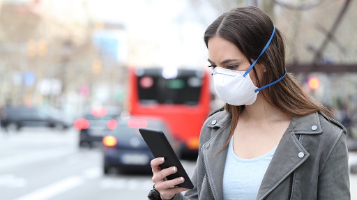Woman with mask using phone with city traffic background