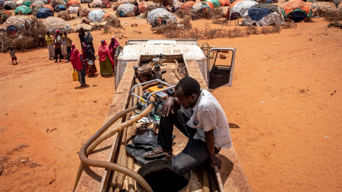 Nella foto: Somalia. In cima a una cisterna, un uomo aspetta che l'acqua venga pompata nella borsa. Fonte: Al Jazeera.
